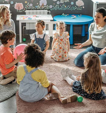 young children in a circle having a discussion led by teachers