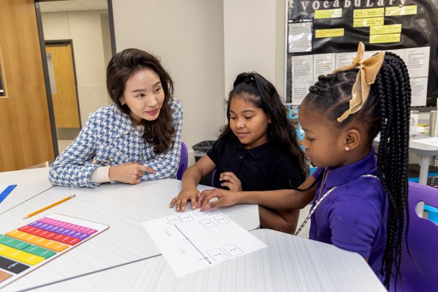 Teacher and two students sit around a table in a classroom 