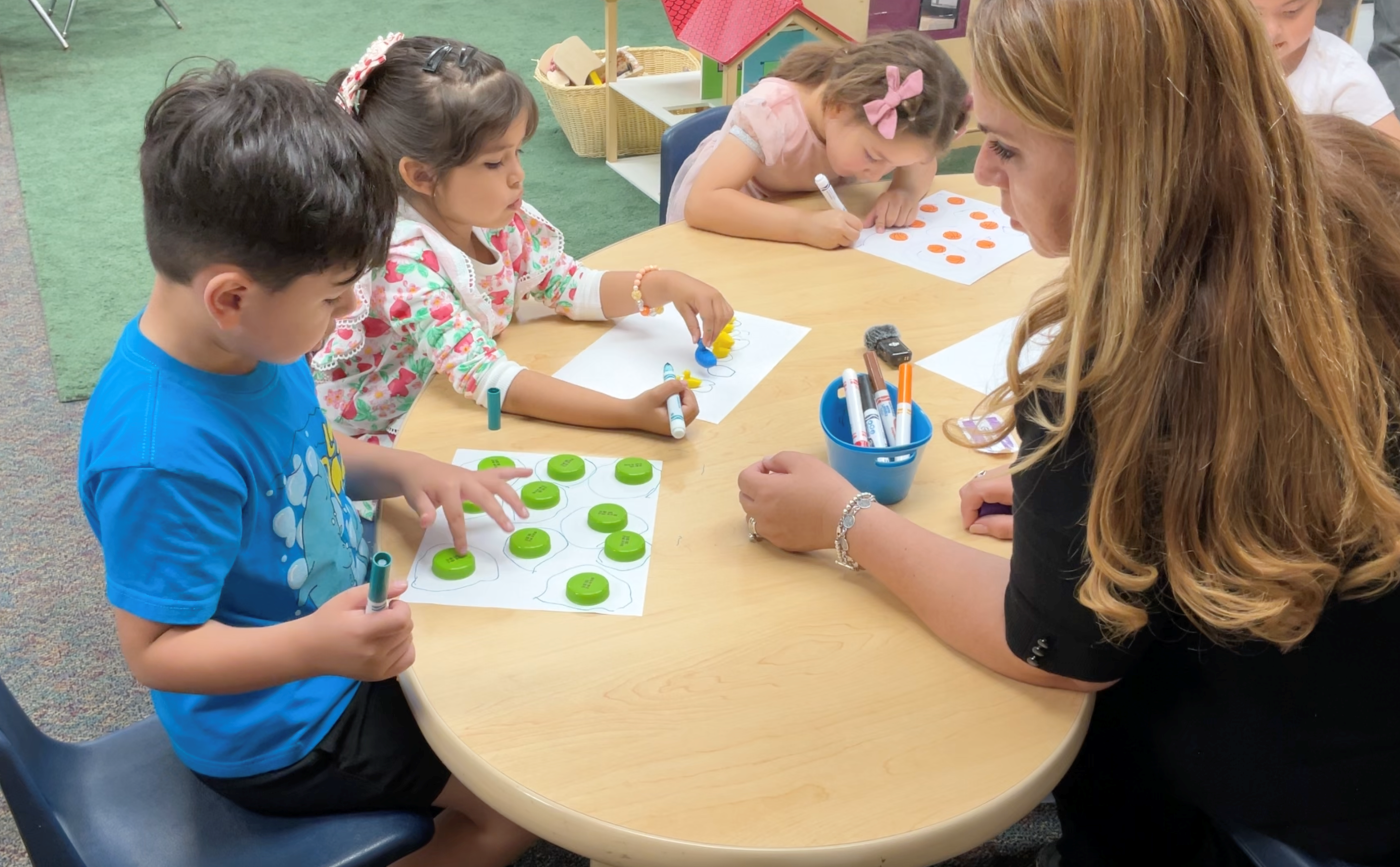 Teacher and students sitting around a classroom table using math manipulatives.